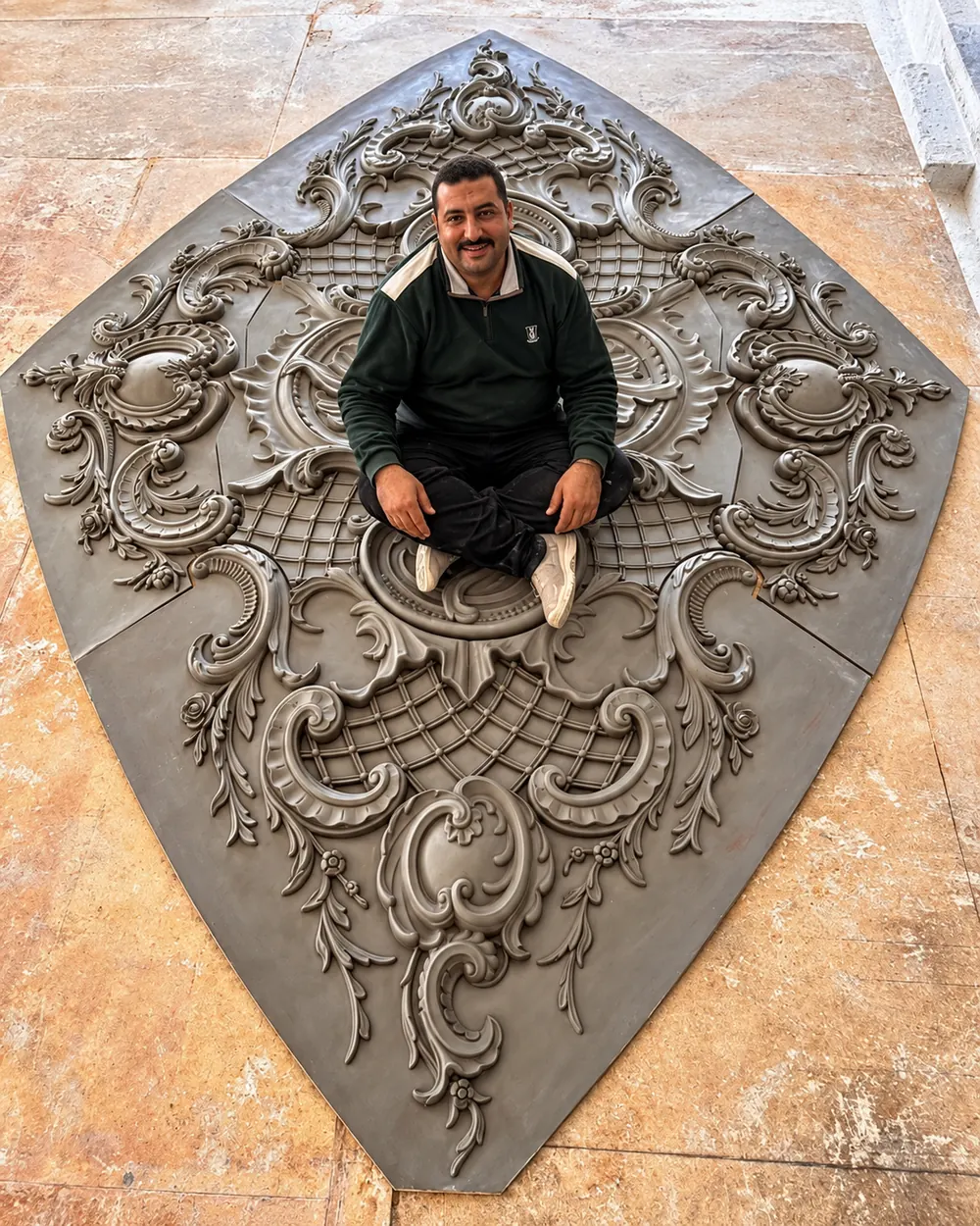 A large scrolled ornament laid out on the floor before fixing
