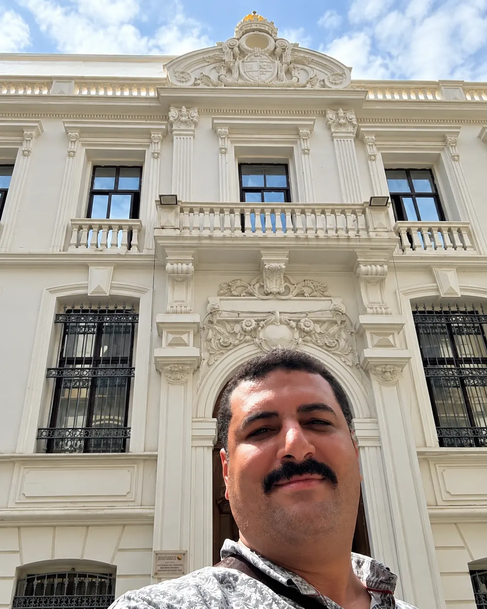On site in front of a cream façade with a carved balcony
